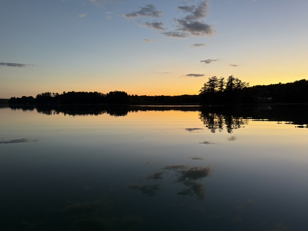 Golden dusk over Threemile Pond with tree-lined shoreline reflections